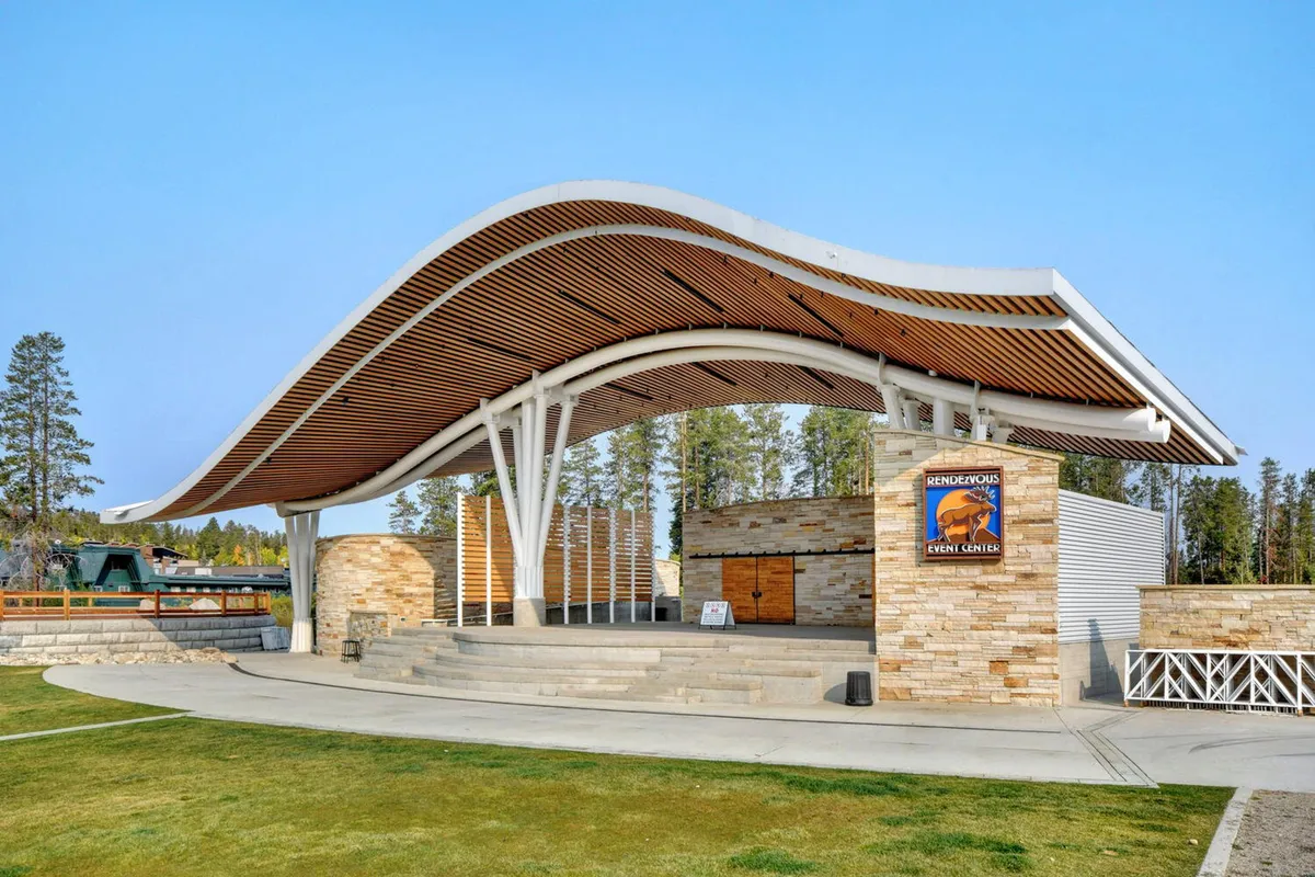 A distinctive outdoor venue featuring a wave-like roof structure, stone façade, and wooden accents—suggesting an area for community gatherings and local events. The setting is festive, inviting, and indicative of neighborhood attractions close to the property.
