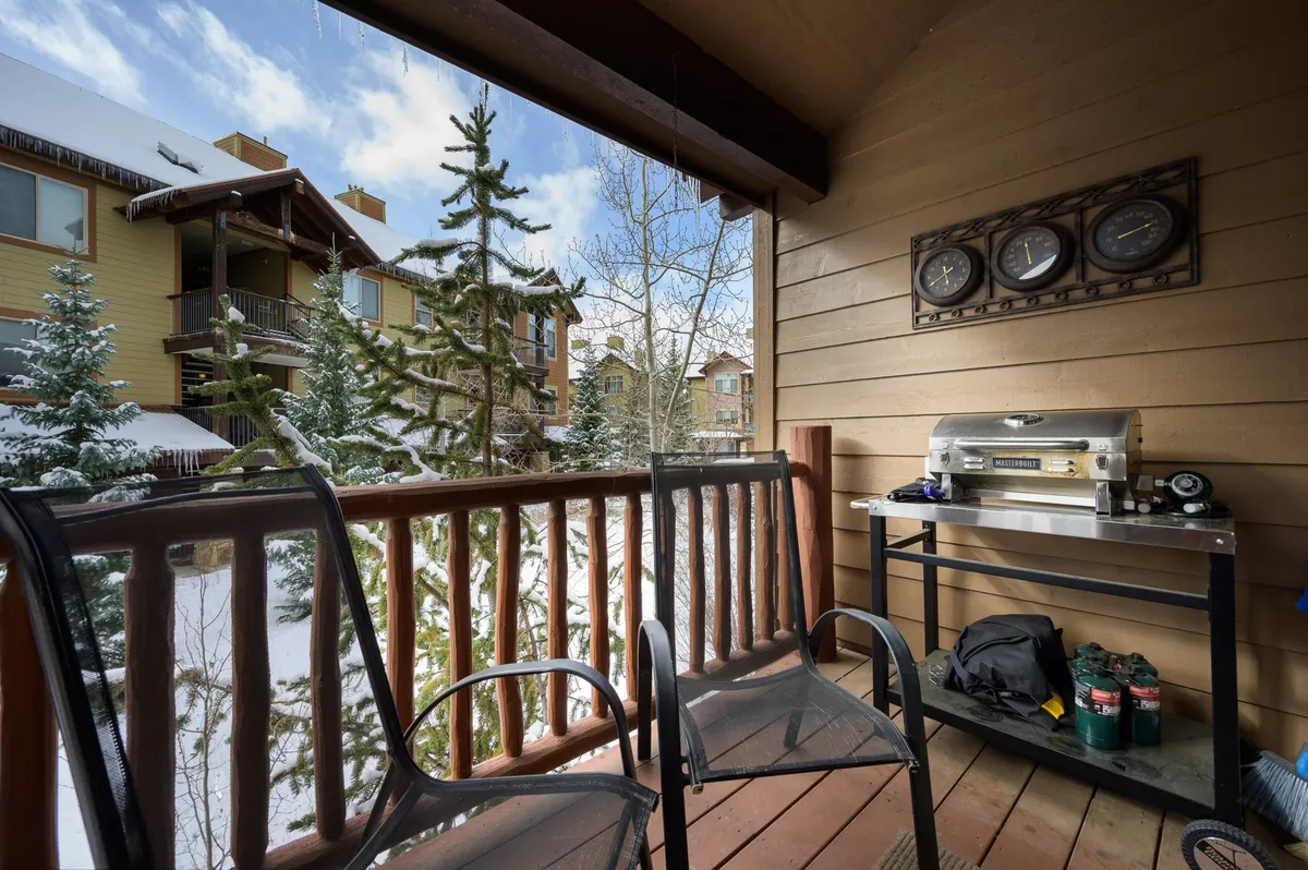 This image features two chairs positioned on a private balcony, a grill, snow-covered trees, and nearby buildings. The setting evokes a peaceful, scenic spot for guests to relax and take in the mountain atmosphere, with clear outdoor seating and winter views.