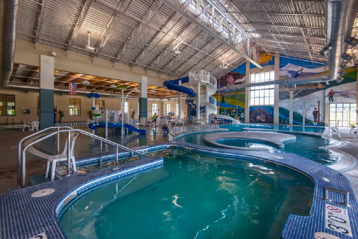 A lively indoor recreation center with water slides, a swimming pool, colorful murals, and play areas for families and children. The atmosphere is joyful and energetic, ideal for active family fun just steps away from home.