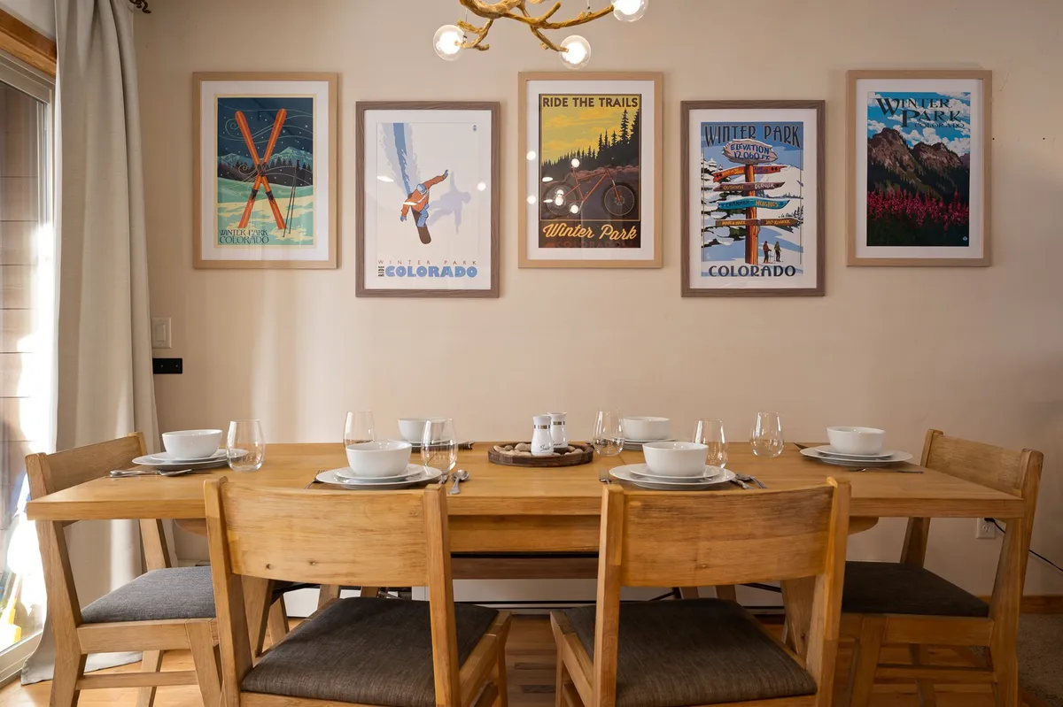 A stylish dining area featuring a large table surrounded by chairs, decorative wall art, a striking chandelier, and a window offering scenic views. The space is arranged for group meals, conversations, and celebrations, capturing the warmth and togetherness described in the section.