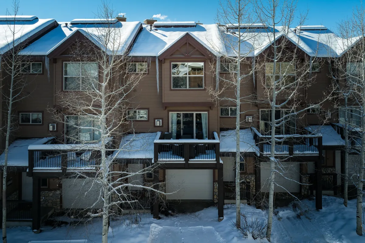 The photo captures the welcoming townhouse facade surrounded by aspen trees and snow, with visible balconies where guests can watch snow fall or enjoy time together. The cozy exterior hints at the vibrant life within and the community atmosphere.