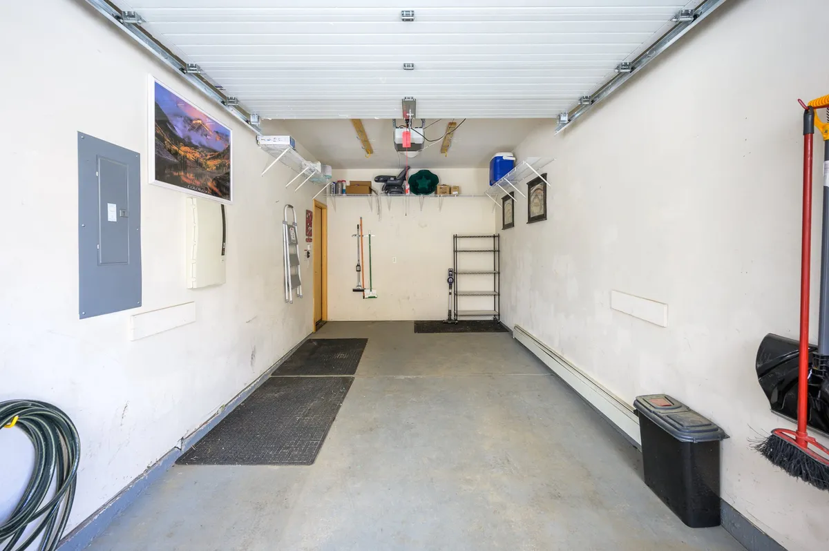 A spacious garage area with a clean floor, storage shelves, and wall-mounted tools. The space is organized and designed for vehicle parking, gear storage, and home maintenance, reflecting ample storage and readiness for outdoor activities.