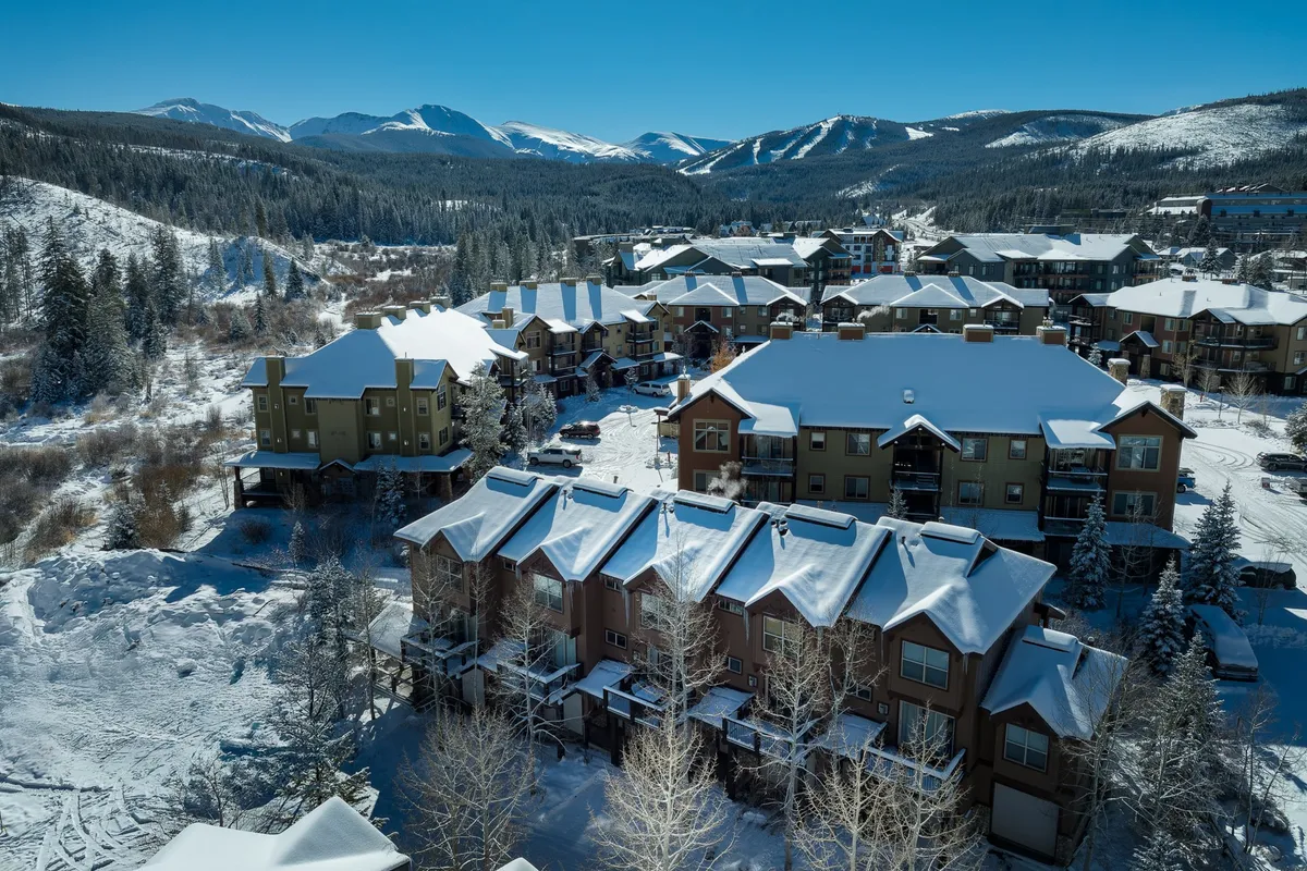 A wide view of snow-covered rooftops nestled in a valley, with a stunning mountain backdrop and a cluster of charming buildings. The landscape exudes tranquility and showcases the neighborhood's proximity to scenic outdoor areas.