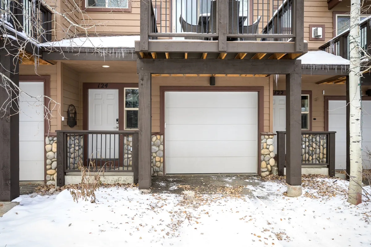 A welcoming exterior shot of the townhome, showing the wooden balcony, stone accents, and snow-dusted ground. The inviting setting hints at cozy evenings inside and easy access to outdoor fun.